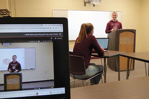 student speaking to another student at a podium while being recorded on a laptop